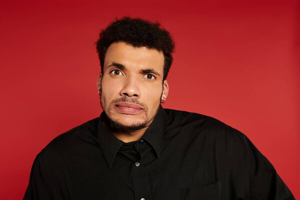 A young, confident man with a playful look stands against a bright red background.