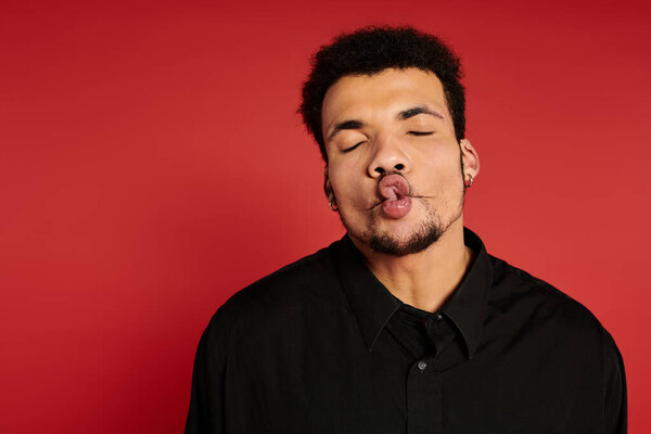 Молодой человек с очаровательной улыбкой и игривым выражением лица стоит на ярком красном фоне.