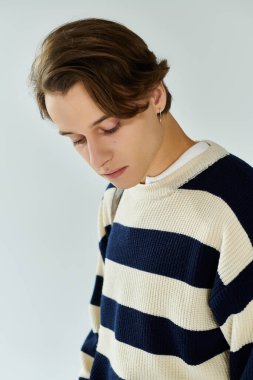 Şık çizgili süveter giyen genç bir adam üniversite deneyimini stüdyoda yansıtıyor..