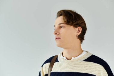 Çizgili bir süveter giyen genç bir adam düşünceli, genç ve hırslı görünüyor..