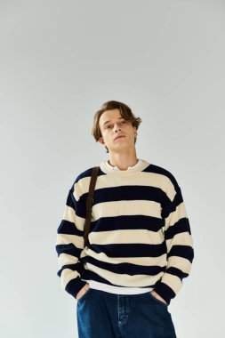 Çizgili süveter giyen genç bir adam, elleri ceplerinde, koleje gitmek için hazır bekliyor..