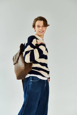 Çizgili süveter giyen yakışıklı genç bir adam stüdyo boşluğunda güvenle duruyor..