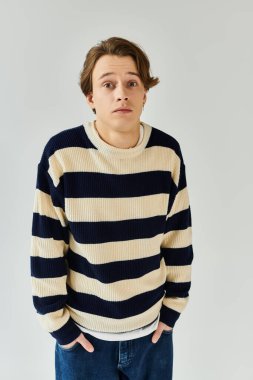 Şık bir genç adam çizgili bir süveter içinde kendine güvenerek duruyor, genç modasını somutlaştırıyor..