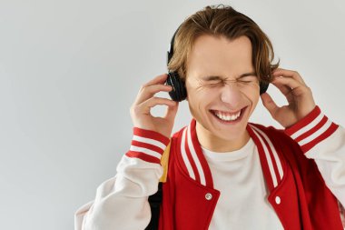 Handsome young man in a bomber jacket smiles with joy while listening to music in a studio. clipart