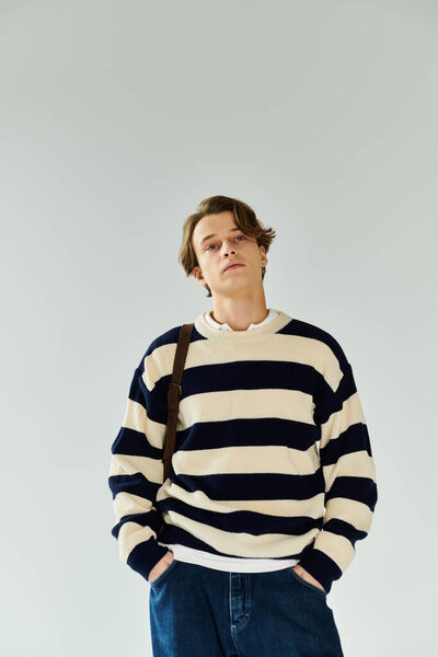 Молодой человек в полосатом свитере уверенно стоит с руками в карманах, готовый к поступлению в колледж.