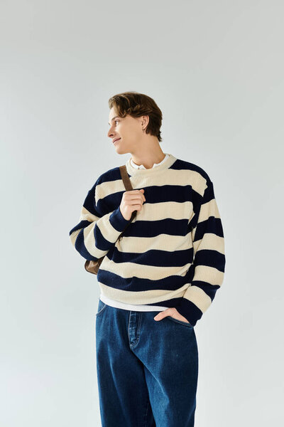 Молодой человек в полосатом свитере задумчиво стоит в современной студии, источая молодость.