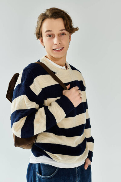 Красивый молодой человек в полосатом свитере уверенно позирует в студии.