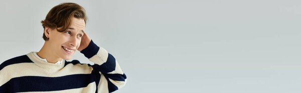 Очаровательный молодой человек в полосатом свитере тепло улыбается, олицетворяя молодежную культуру колледжа, баннер