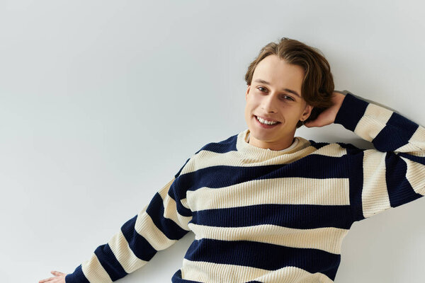 Стильный молодой человек с уверенностью позирует в полосатом свитере, воплощая молодежную культуру.