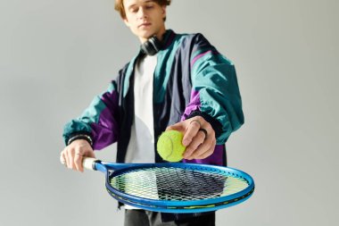 Moda bombardıman ceketli yakışıklı genç adam şık bir stüdyoda tenis topuna vurmaya hazırlanıyor..