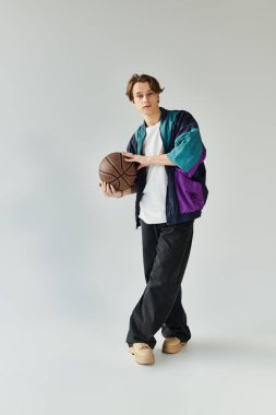 A young man in a trendy bomber jacket stands confidently holding a basketball in a studio. clipart