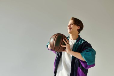 Havalı bir bombardıman ceketi giyen genç bir adam bir stüdyoda neşeyle basketbol topu tutuyor..