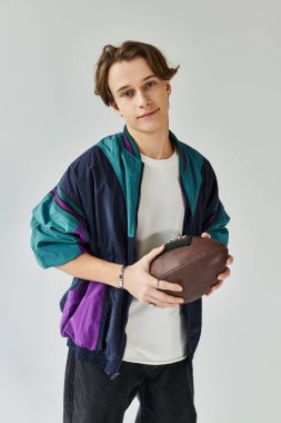 Bombacı ceketi giymiş şık bir genç adam elinde futbol topu tutarken rahatça poz veriyor..