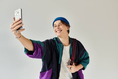 Parlak ve neşeli genç adam şık bir bombacı ceketiyle selfie çekerken gülümsüyor..