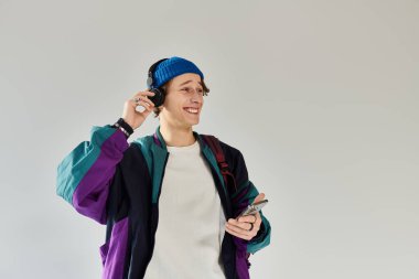 Renkli bir ceket giyen genç bir adam stüdyoda müzik dinlerken gülümsüyor..