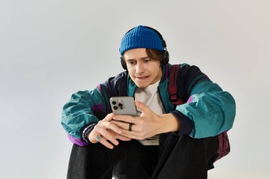 Bombacı ceketi giymiş genç bir adam yerde oturmuş, akıllı telefonuna odaklanmış..