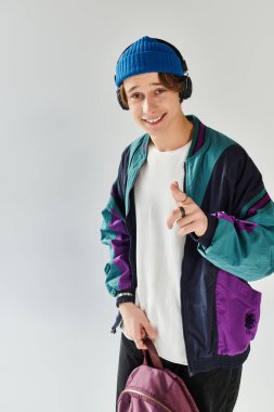 A handsome young man wears a stylish bomber jacket and beanie while smiling in a bright studio. clipart