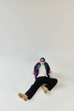 Genç bir adam modaya uygun bombacı ceketini şık bir stüdyoda öylesine otururken gösteriyor..