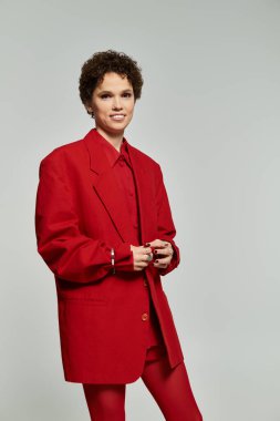 Kendine güvenen genç bir kadın, şık bir kırmızı elbiseyle tarafsız bir arkaplanda sersemletiyor..