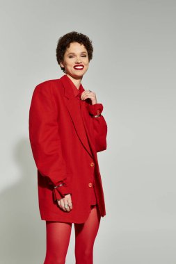 Şık kırmızı elbiseli, kendine güvenen genç bir kadın şık bir stüdyoda zarifçe poz veriyor..