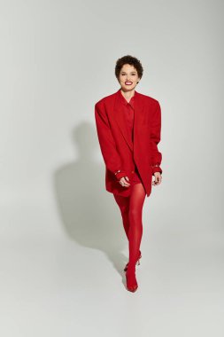 Kendinden emin genç bir kadın canlı kırmızı bir kıyafet ve şık topuklularla önde yürüyor..