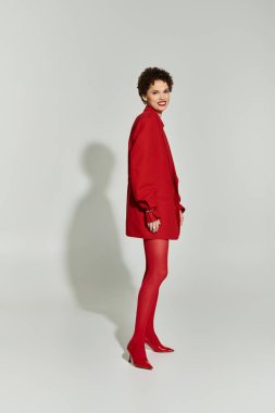 Çarpıcı kırmızı kıyafetli genç bir kadın, sade bir arkaplana karşı güvenle poz veriyor..