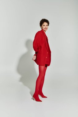 Kendine güvenen genç bir kadın, kırmızı bir elbise içinde yumuşak bir zemine karşı poz veriyor..