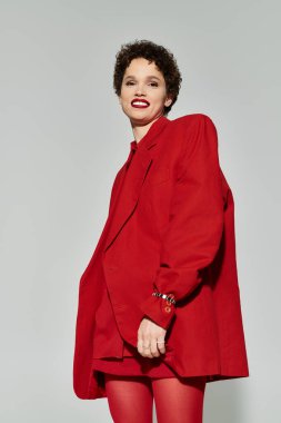 Kırmızı kıyafetli genç bir kadın sade bir arkaplana karşı güven yayıyor..