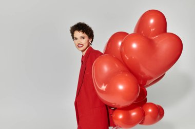 Güzel, genç bir kadın elinde bir demet kırmızı kalp şeklinde balon tutarken gülümsüyor..