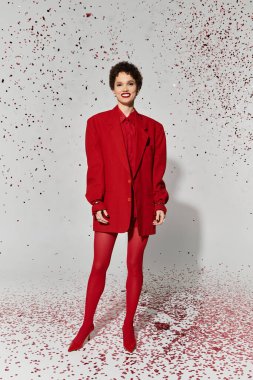 Genç bir kadın, renkli konfetilerle çevrili koyu kırmızı bir kıyafete güvenir..