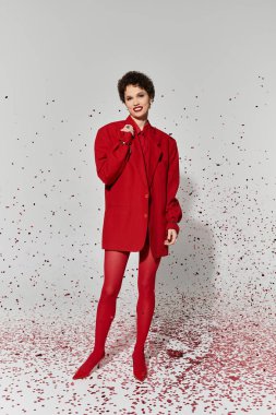 Cesur kırmızı kıyafetli kendine güvenen genç bir kadın neşeyi renkli bir konfetiyle kutluyor..