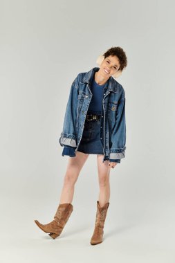 Kendine güvenen genç bir kadın şık bir kot ceket, etek ve kovboy çizmeleri modelliyor..