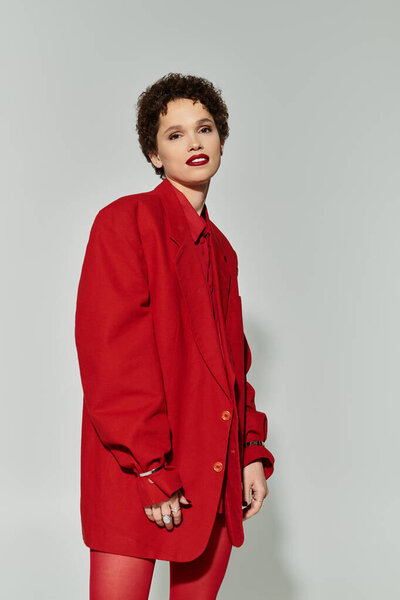 Young woman in a striking red outfit stands confidently against a gray background.
