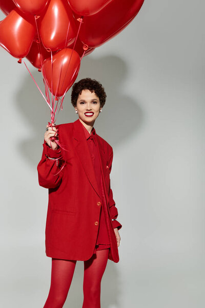 Молодая красивая женщина держит яркие красные воздушные шары, одетые в модную одежду, создавая радость.