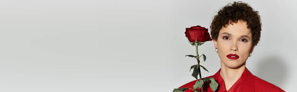 Молодая женщина демонстрирует элегантность в ярко-красной одежде, держа одну розу изящно.