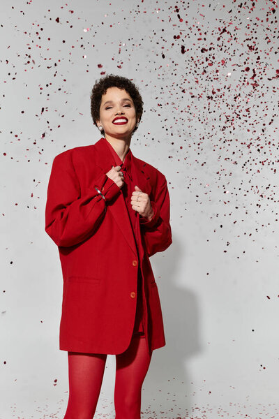 Молодая красивая женщина излучает уверенность в ярком красном наряде, радуясь.