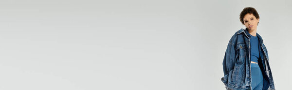 A young beautiful woman poses confidently in a trendy denim outfit against a light backdrop.