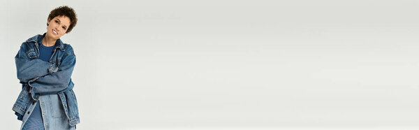 Уверенная в себе молодая женщина моделирует стильный джинсовый наряд на фоне простого рюкзака.