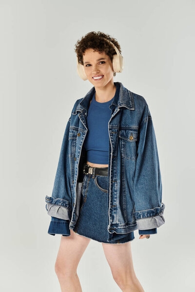 A young woman confidently wears a denim jacket and headphones, radiating joy.