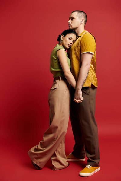 Молодая пара одета модно разделяет нежный момент на ярком студийном фоне.