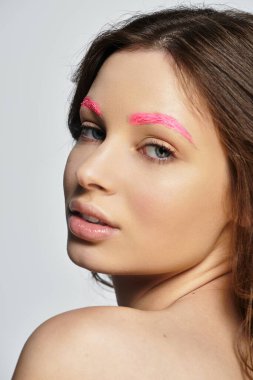 Genç bir kadın canlı pembe kaşlarını sergiliyor, stüdyo ışığı altında çarpıcı bir stili kucaklıyor..