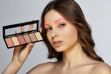 Attractive young woman flaunts her pink eyebrows and bold makeup in a studio setting. clipart