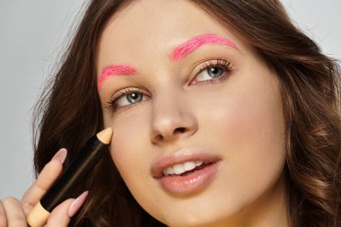 Attractive young woman with pink eyebrows highlights her bold style while applying makeup. clipart