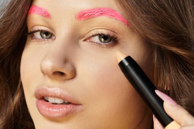 Pembe kaşlı genç kadın, gri bir zemine karşı cesur bir moda sergiliyor..