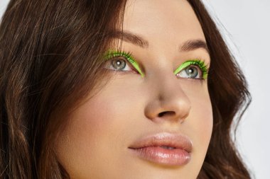 A striking young woman showcases her beauty with bold green eyeshadow on a grey backdrop. clipart