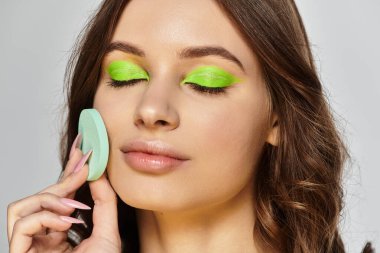 A young woman showcases her beauty with bold green eyeshadow and flawless makeup in a studio. clipart