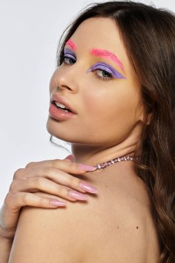 Genç bir kadın sanatsal makyajını mor göz farı ve pembe kaşlarıyla sergiliyor..