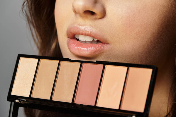 Молодая женщина демонстрирует свою палитру макияжа на сером фоне.