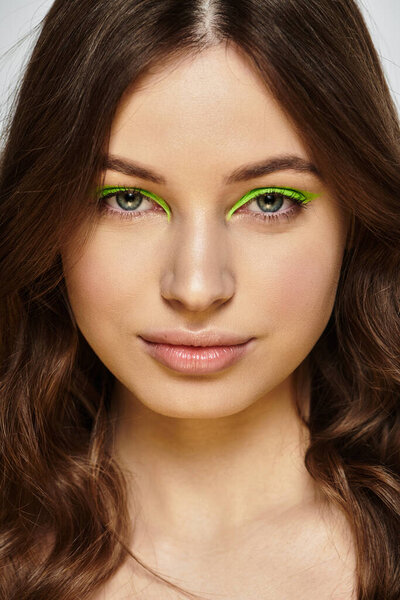 Young woman showcases bold beauty with striking green eyeshadow against a grey backdrop.