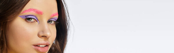 Молодая женщина демонстрирует свою смелую красоту с яркими фиолетовыми тенями для век и розовыми бровями, баннером
